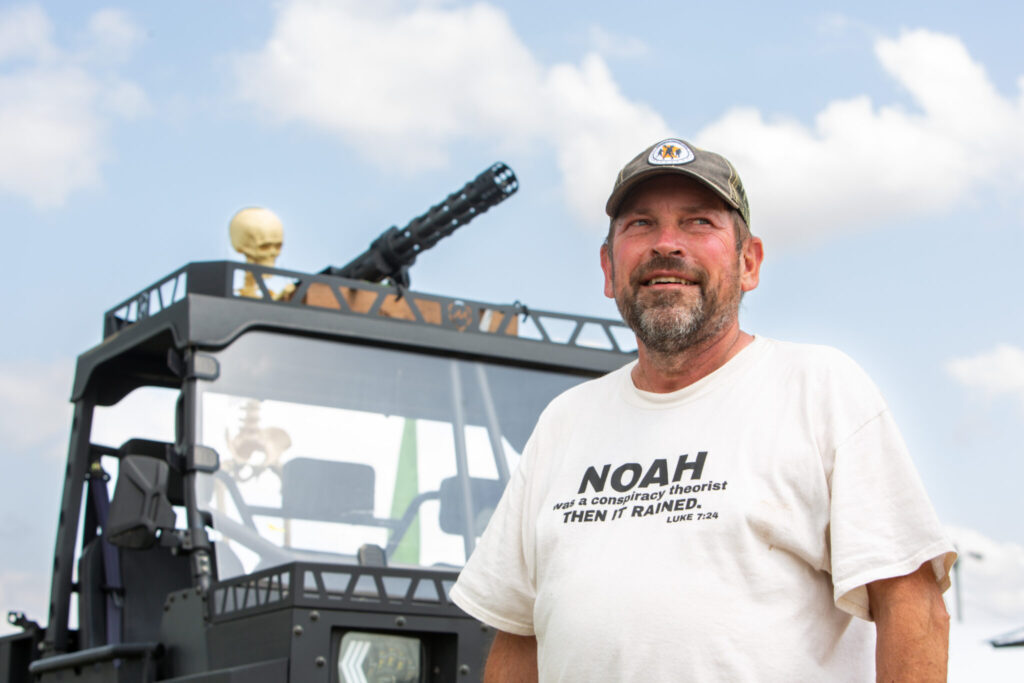 Troy McKinley, organizer of the Minnesota Prepper Expo, poses for a portrait with the cart he affixed with skeletons at the Minnesota Prepper Expo at the Morrison County Fairgrounds in Little Falls, Minnesota, on Saturday, June 21, 2025. (Photo by Nicole Neri/Minnesota Reformer)